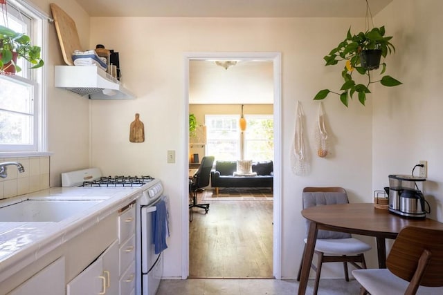 interior space featuring white gas range oven, white cabinets, tile countertops, light wood-type flooring, and sink