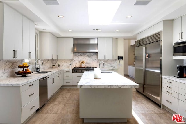 kitchen with built in appliances, light tile floors, a center island, wall chimney range hood, and sink