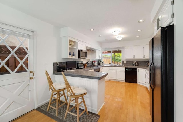 kitchen featuring white cabinets, a kitchen bar, black appliances, light hardwood / wood-style flooring, and kitchen peninsula