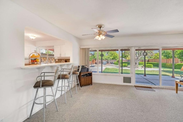 interior space with ceiling fan, a wealth of natural light, light carpet, and white cabinetry