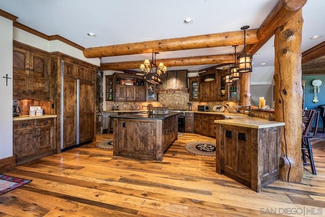 kitchen with an island with sink, a notable chandelier, decorative light fixtures, light hardwood / wood-style flooring, and wall chimney exhaust hood