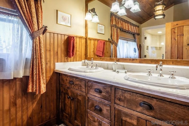 bathroom with double sink, wood walls, oversized vanity, and vaulted ceiling