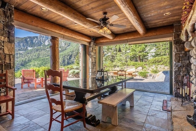 sunroom featuring ceiling fan, a mountain view, a healthy amount of sunlight, wooden ceiling, and beam ceiling