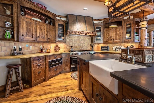 kitchen featuring light hardwood / wood-style floors, double oven range, tasteful backsplash, wall chimney exhaust hood, and pendant lighting