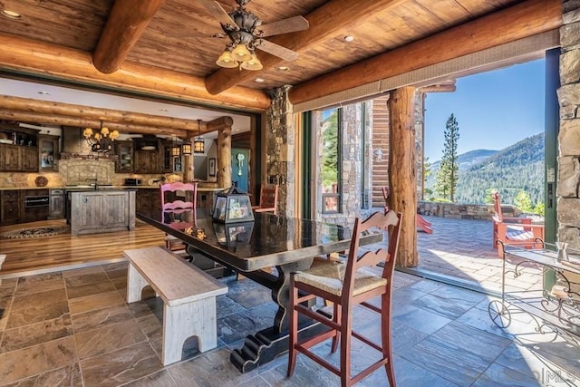 dining space with ceiling fan with notable chandelier, dark tile floors, a mountain view, beam ceiling, and wood ceiling