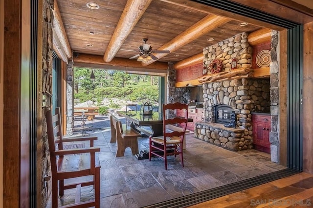 unfurnished dining area with wooden ceiling, a stone fireplace, ceiling fan, and beamed ceiling