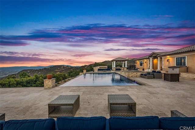 pool at dusk featuring outdoor lounge area, a patio, and a gazebo