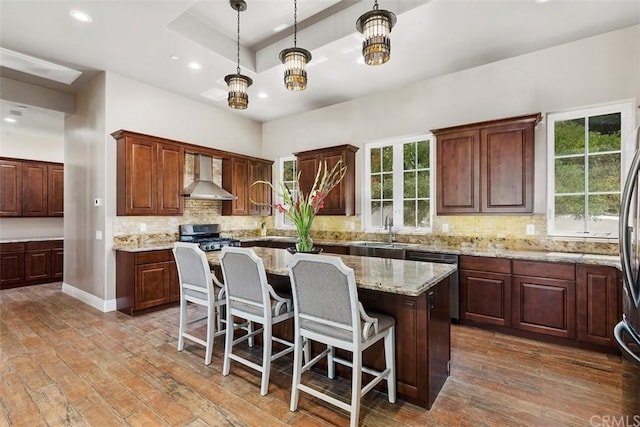 kitchen featuring pendant lighting, a kitchen island, wall chimney range hood, tasteful backsplash, and wood-type flooring