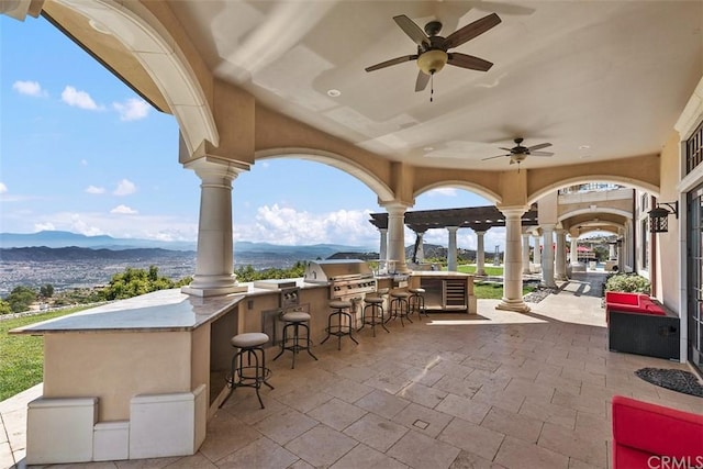 view of terrace featuring an outdoor bar, ceiling fan, a mountain view, a grill, and area for grilling