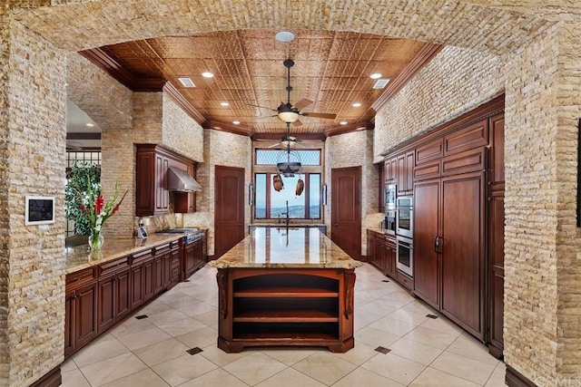 kitchen featuring ceiling fan, light tile flooring, stainless steel appliances, a center island, and light stone counters