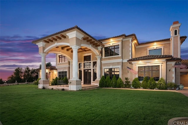 back house at dusk featuring a lawn and a garage