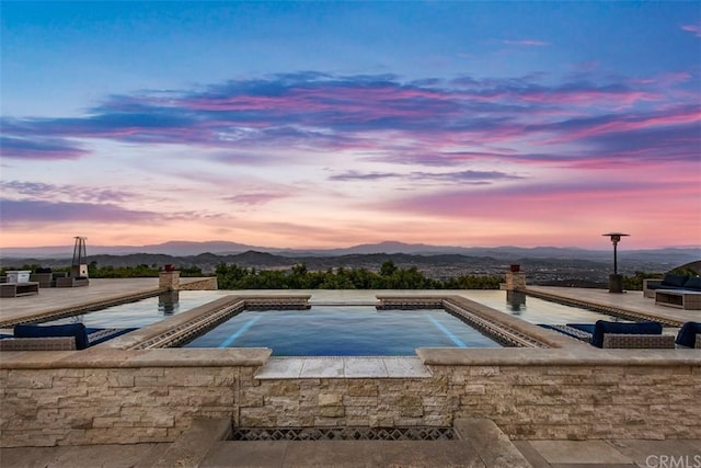 pool at dusk featuring a mountain view and a hot tub