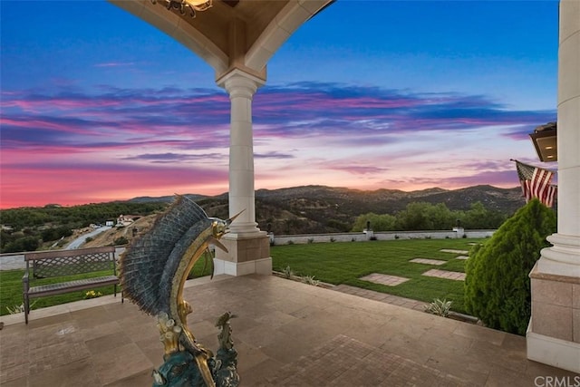 patio terrace at dusk featuring a mountain view and a yard