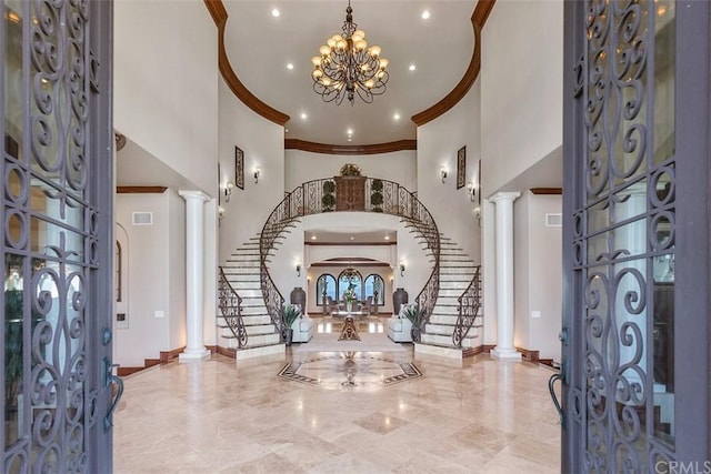 foyer with french doors, decorative columns, a towering ceiling, and an inviting chandelier