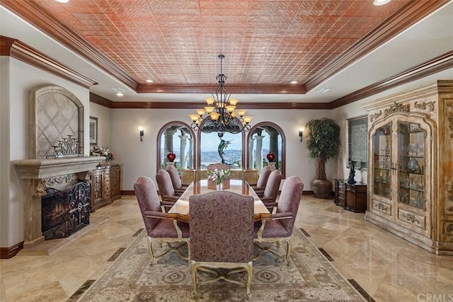 dining room with an inviting chandelier, a raised ceiling, a fireplace, light tile floors, and ornamental molding