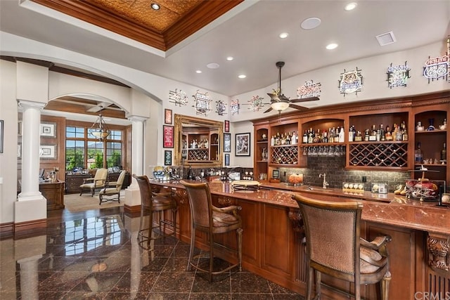 bar featuring backsplash, dark tile floors, pendant lighting, ceiling fan, and decorative columns