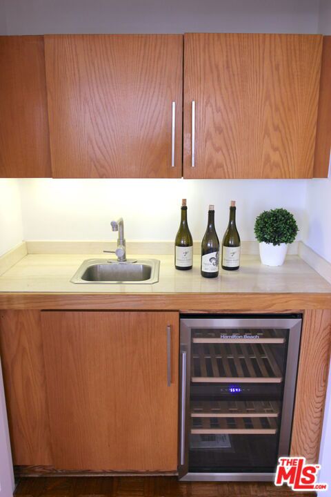 bar with wine cooler, dark wood-type flooring, and sink