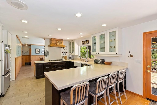 kitchen featuring kitchen peninsula, premium range hood, white cabinets, appliances with stainless steel finishes, and a kitchen breakfast bar