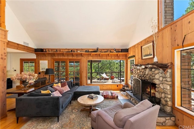 living room featuring french doors, wooden walls, high vaulted ceiling, a fireplace, and hardwood / wood-style flooring