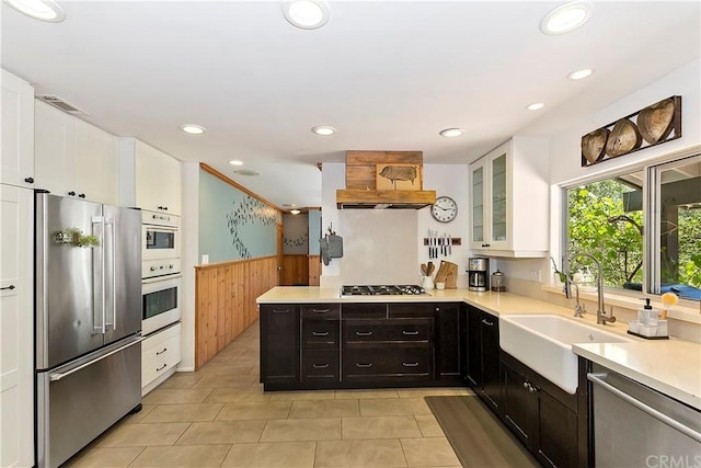 kitchen with white cabinets, wood walls, stainless steel appliances, sink, and dark brown cabinets