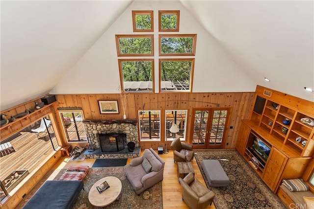 living room with wooden walls, a fireplace, french doors, hardwood / wood-style flooring, and high vaulted ceiling