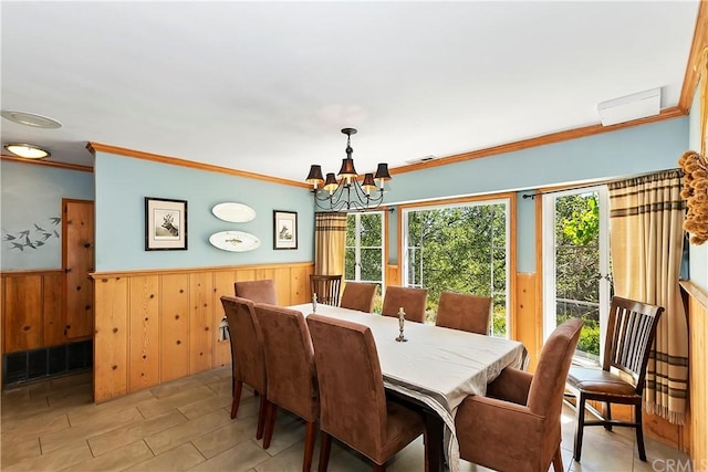 dining area with an inviting chandelier, wood walls, and crown molding