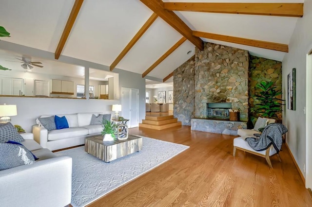 living room featuring a stone fireplace, high vaulted ceiling, ceiling fan, light hardwood / wood-style floors, and beamed ceiling