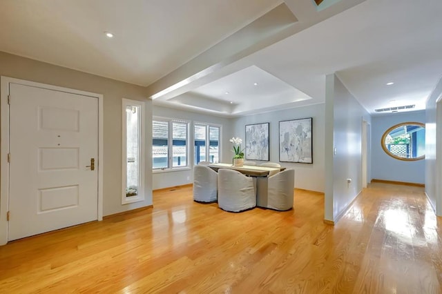 foyer with light wood-type flooring, a raised ceiling, and a wealth of natural light