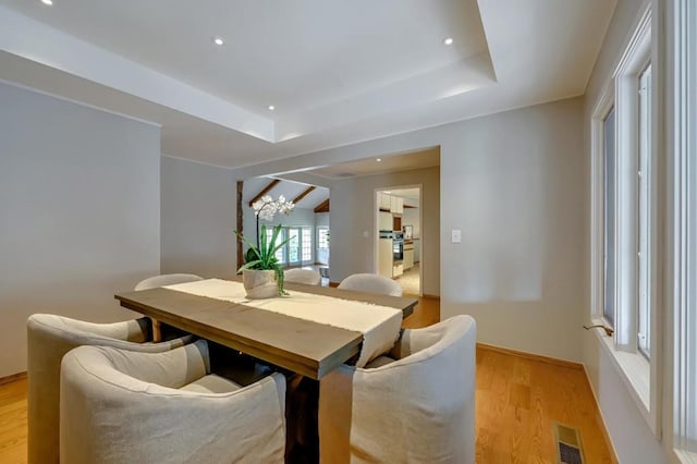 dining space featuring light wood-type flooring, a chandelier, and a tray ceiling