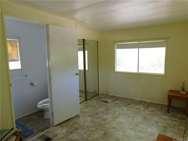 unfurnished bedroom with multiple windows, connected bathroom, and light tile floors