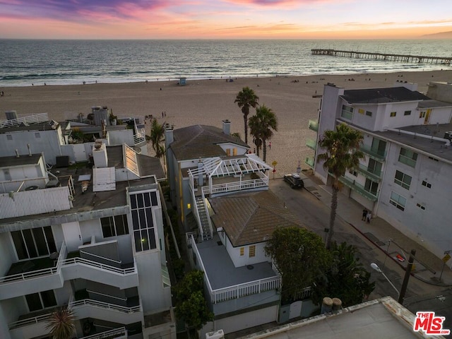 aerial view at dusk featuring a water view and a view of the beach