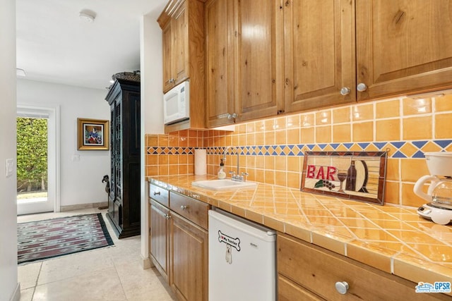 kitchen featuring backsplash, white appliances, sink, light tile patterned floors, and tile counters