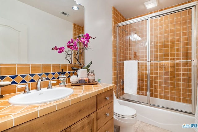 full bathroom featuring tasteful backsplash, vanity, shower / bath combination with glass door, tile patterned flooring, and toilet