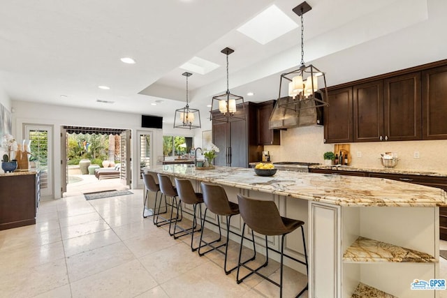 kitchen featuring a skylight, a kitchen breakfast bar, a spacious island, decorative backsplash, and custom exhaust hood