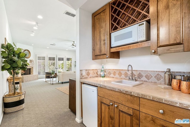 kitchen featuring white appliances, backsplash, sink, ceiling fan, and light colored carpet