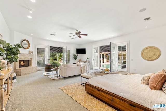 bedroom with access to exterior, ceiling fan, light colored carpet, and a tiled fireplace