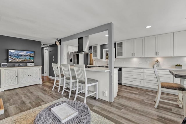 kitchen with island range hood, glass insert cabinets, light countertops, light wood-type flooring, and white cabinetry