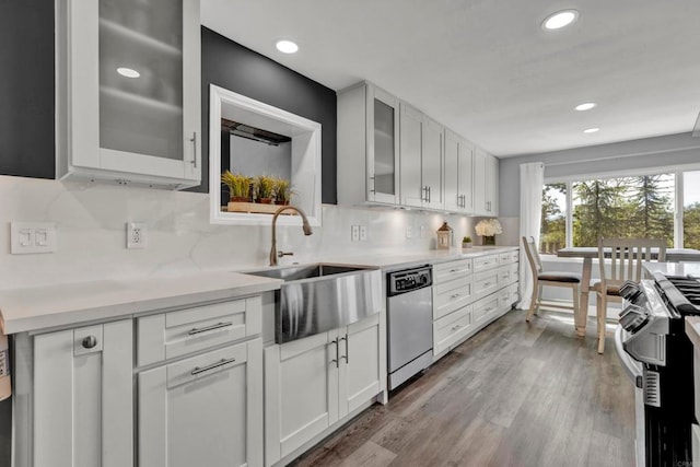 kitchen with glass insert cabinets, white cabinetry, light countertops, stainless steel dishwasher, and gas range