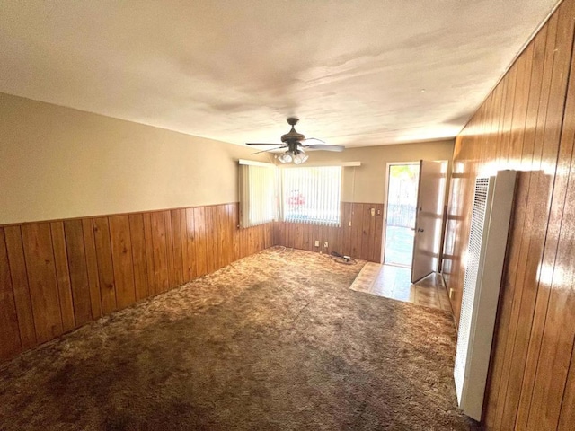 carpeted empty room with wood walls and ceiling fan