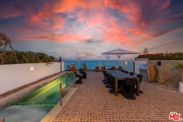 patio terrace at dusk featuring a fenced in pool and a water view