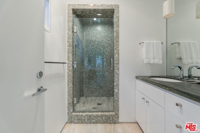 bathroom with walk in shower, wood-type flooring, and vanity with extensive cabinet space