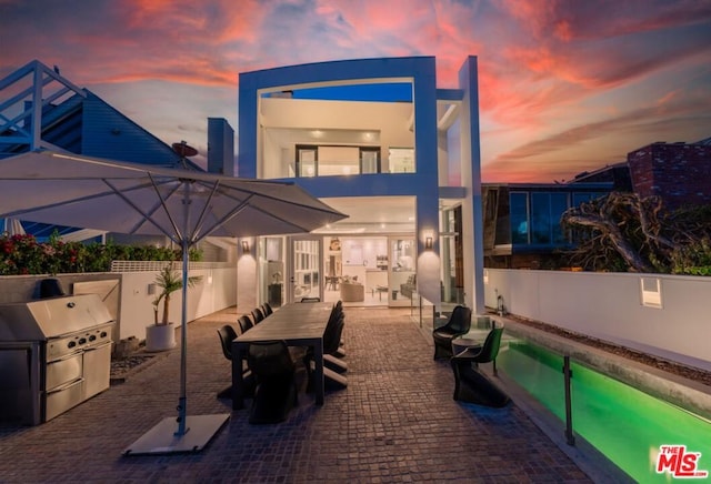 patio terrace at dusk with a grill, area for grilling, and a fenced in pool