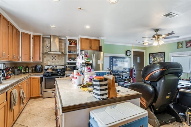 kitchen featuring ceiling fan, appliances with stainless steel finishes, wall chimney range hood, a kitchen island, and tasteful backsplash