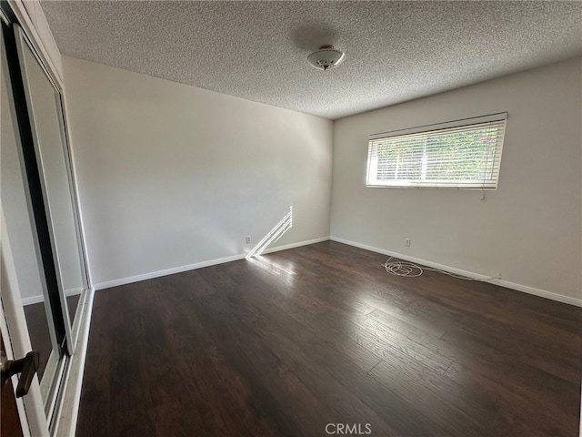 empty room with a textured ceiling, dark wood-style flooring, and baseboards