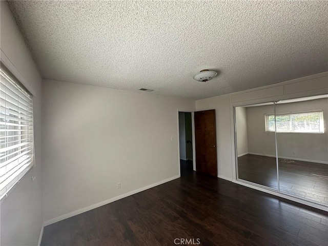 unfurnished bedroom featuring a closet, dark wood-style flooring, a textured ceiling, and baseboards