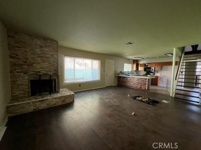 unfurnished living room with visible vents, stairway, dark wood-type flooring, a stone fireplace, and baseboards