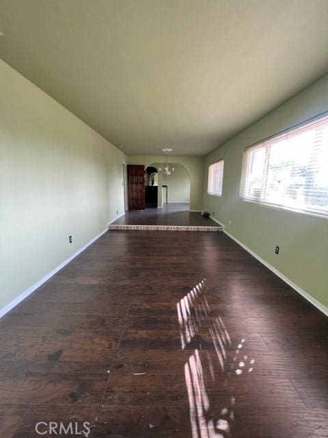 unfurnished living room featuring arched walkways, dark wood-style floors, and baseboards