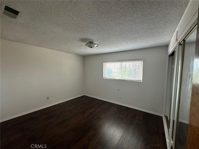 empty room featuring a textured ceiling and dark hardwood / wood-style flooring