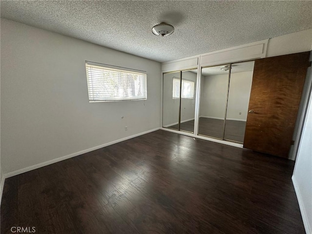 unfurnished bedroom with dark wood-style floors, a textured ceiling, baseboards, and multiple closets