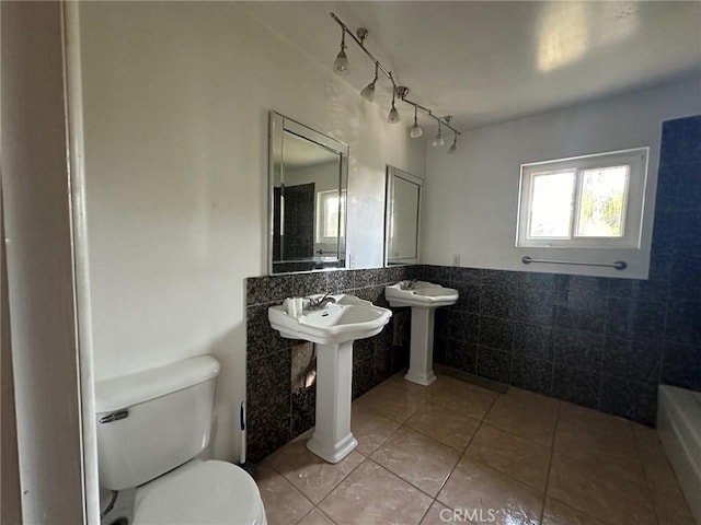 bathroom with a wainscoted wall, tile walls, toilet, a bathing tub, and tile patterned floors